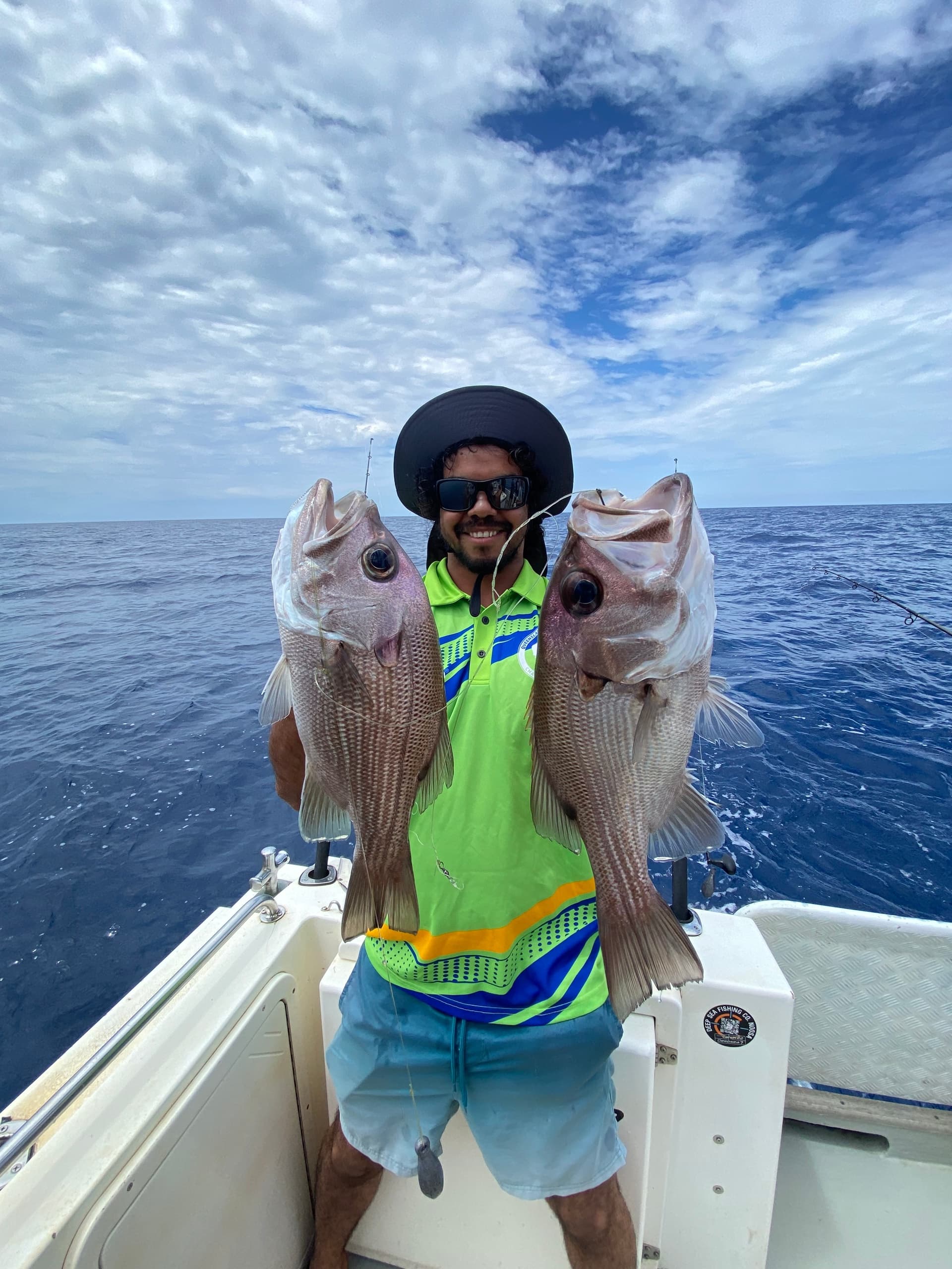 Fisherman holding two large bream on boat under cloudy sky