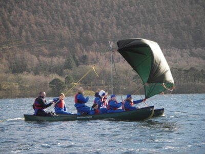 Canoe team sailing with spinnaker on scenic mountain lake