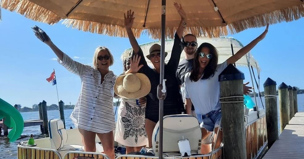 Friends celebrating on tiki boat near dock enjoying sunny coastal boat tour