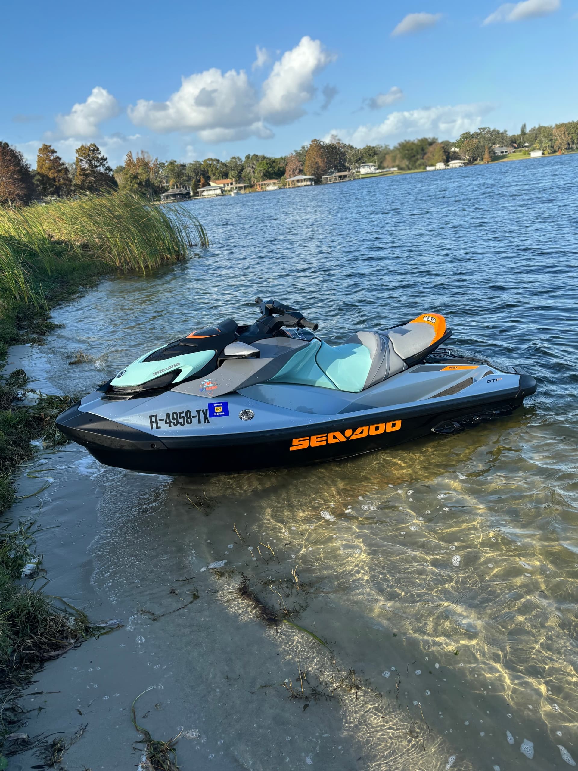 Sea-Doo jet ski on sandy lake shore with trees and blue sky