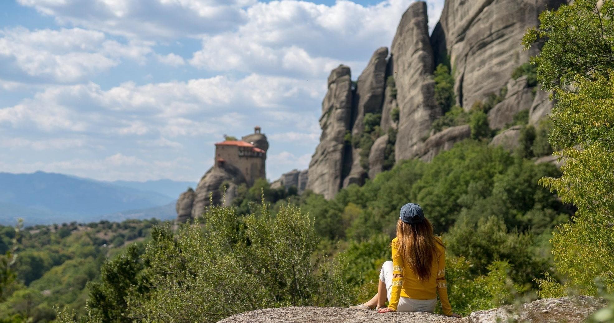 Woman sitting on rock overlooking Meteora cliffs and monastery