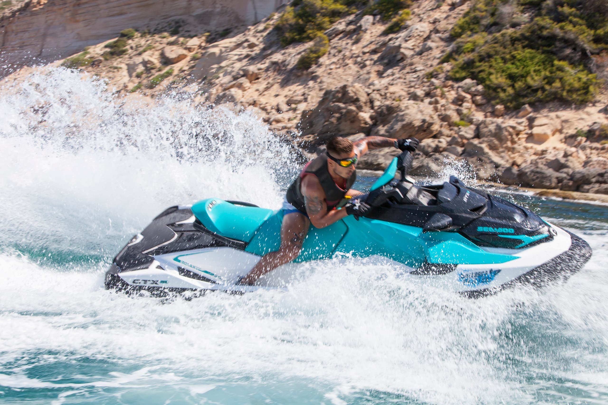 Jet ski rider leaning into a sharp turn by rocky shoreline