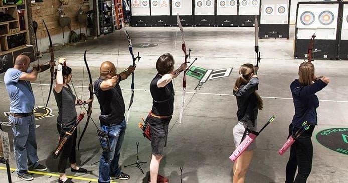 Group practicing archery at indoor Manhattan range, aiming at targets