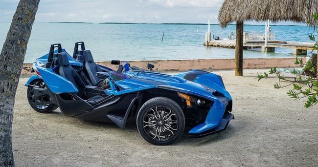 Blue slingshot parked near palm-thatched hut on tropical shoreline