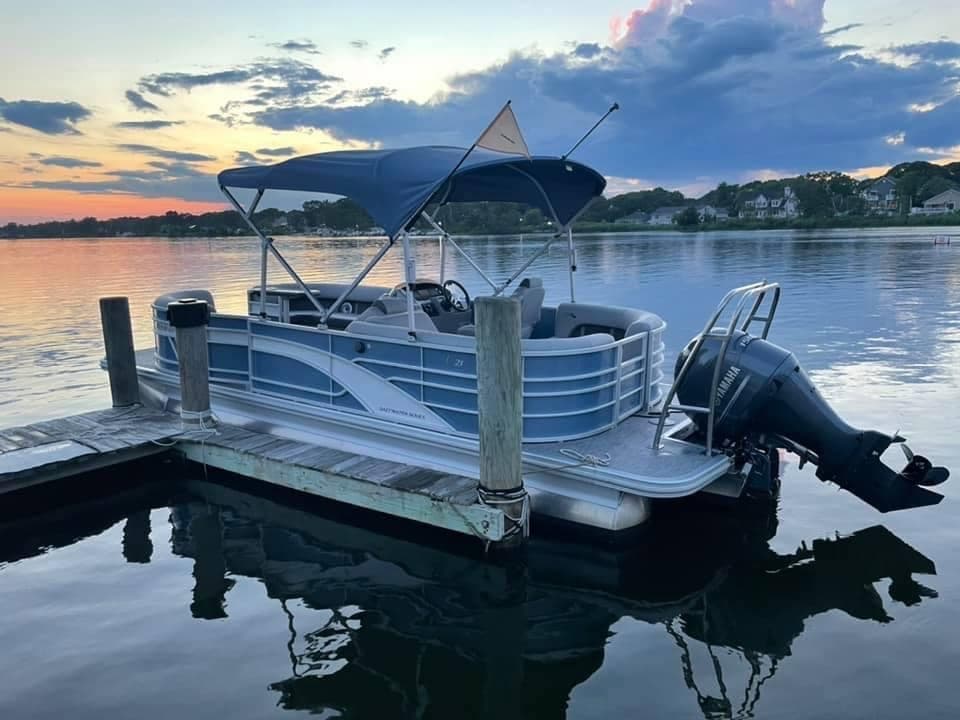 Pontoon boat at dock at sunset with water reflections and sky