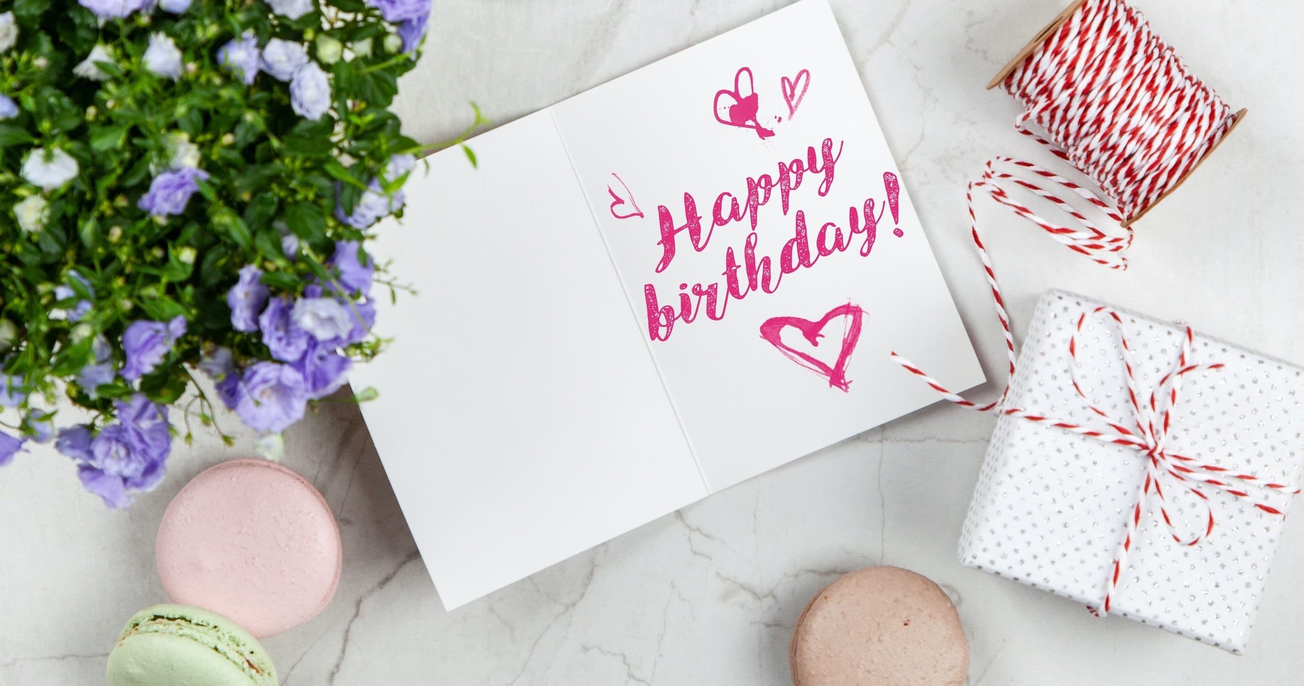 Birthday card and gift on tabletop with macarons and flowers, celebration