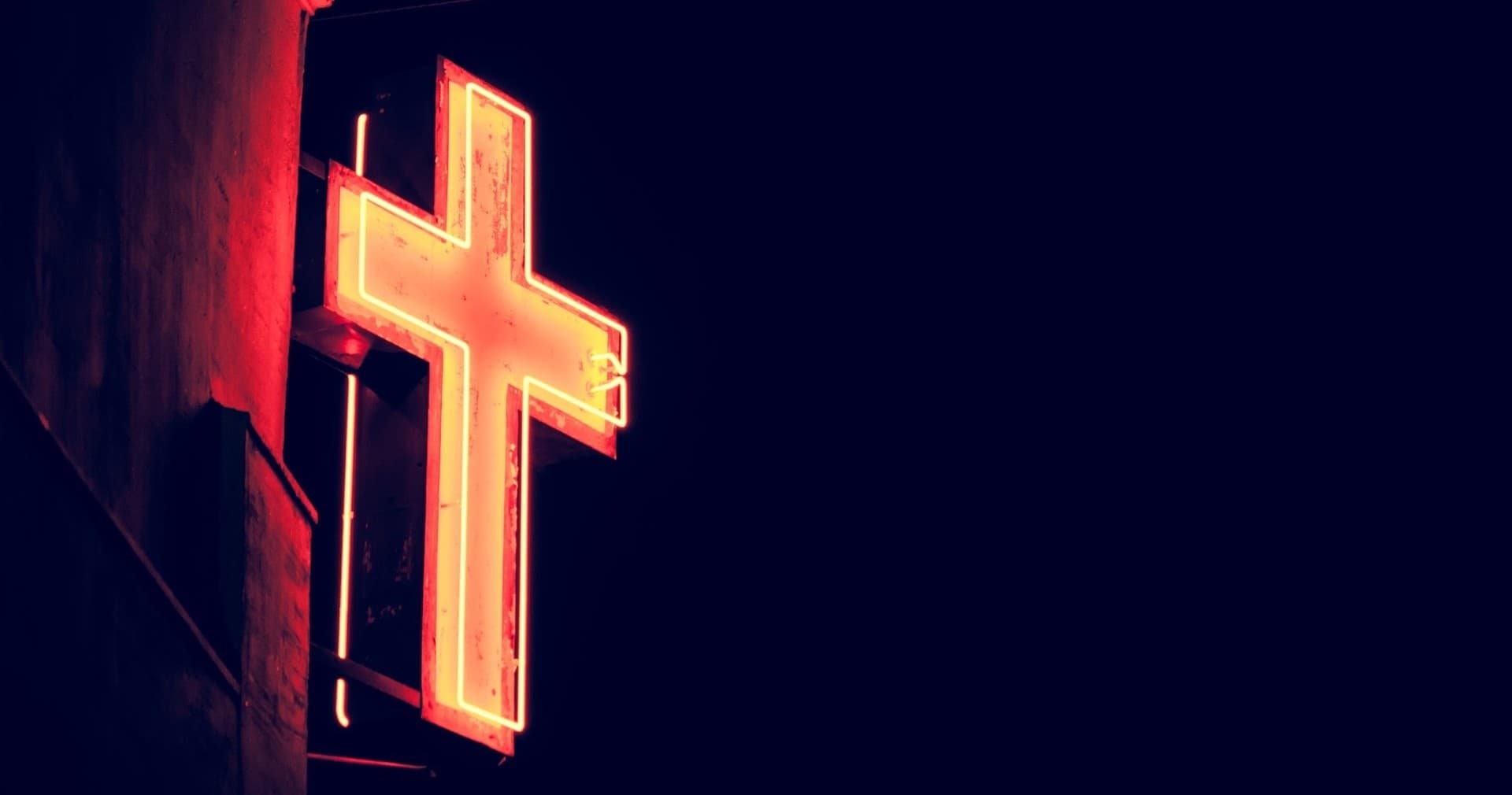 Neon church cross sign glowing at night on facade