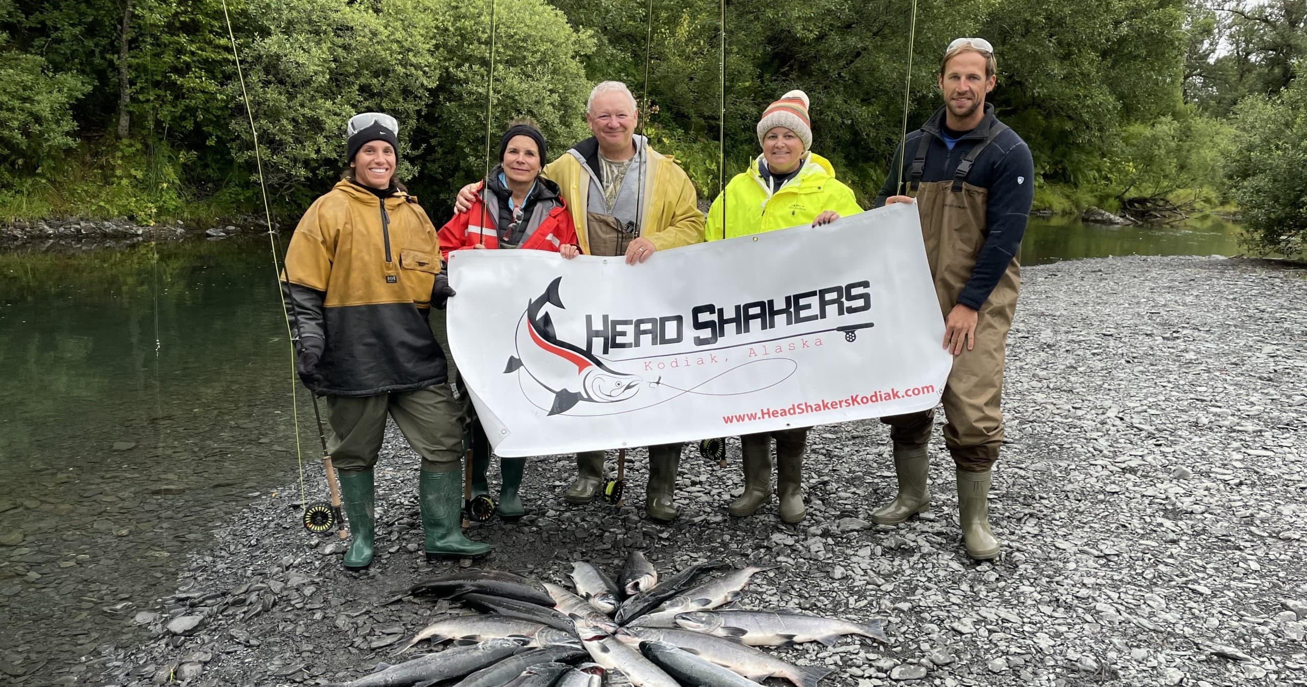 Anglers showing salmon catch on gravel riverbank in Kodiak