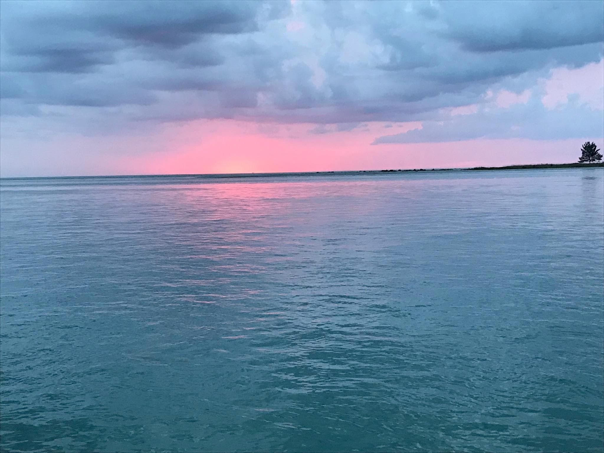 Calm ocean at pink sunset with distant shoreline, serene seascape