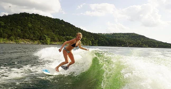 Wakesurfer carving a wave behind boat on hill-backed lake