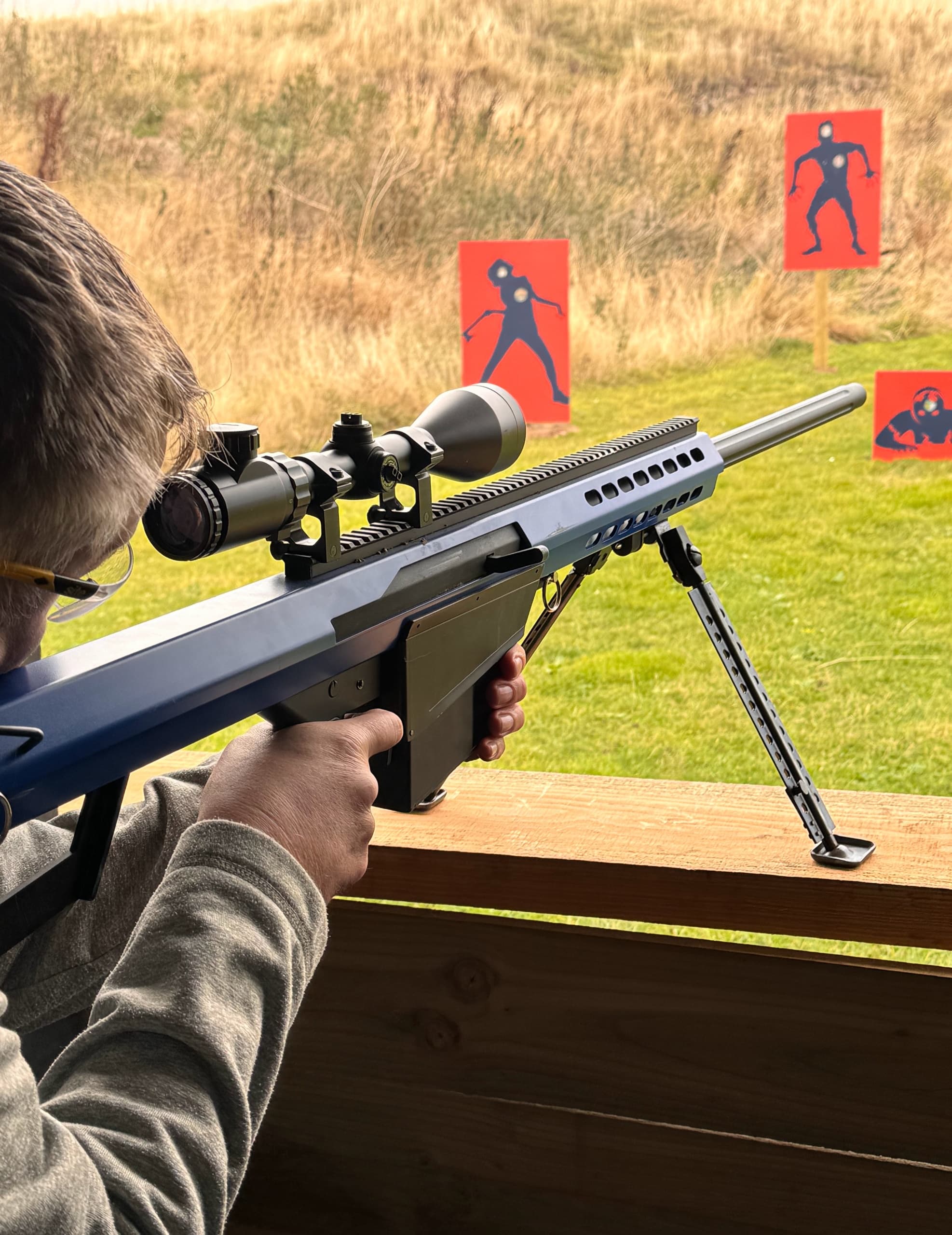 Shooter aiming rifle at outdoor target range with scope