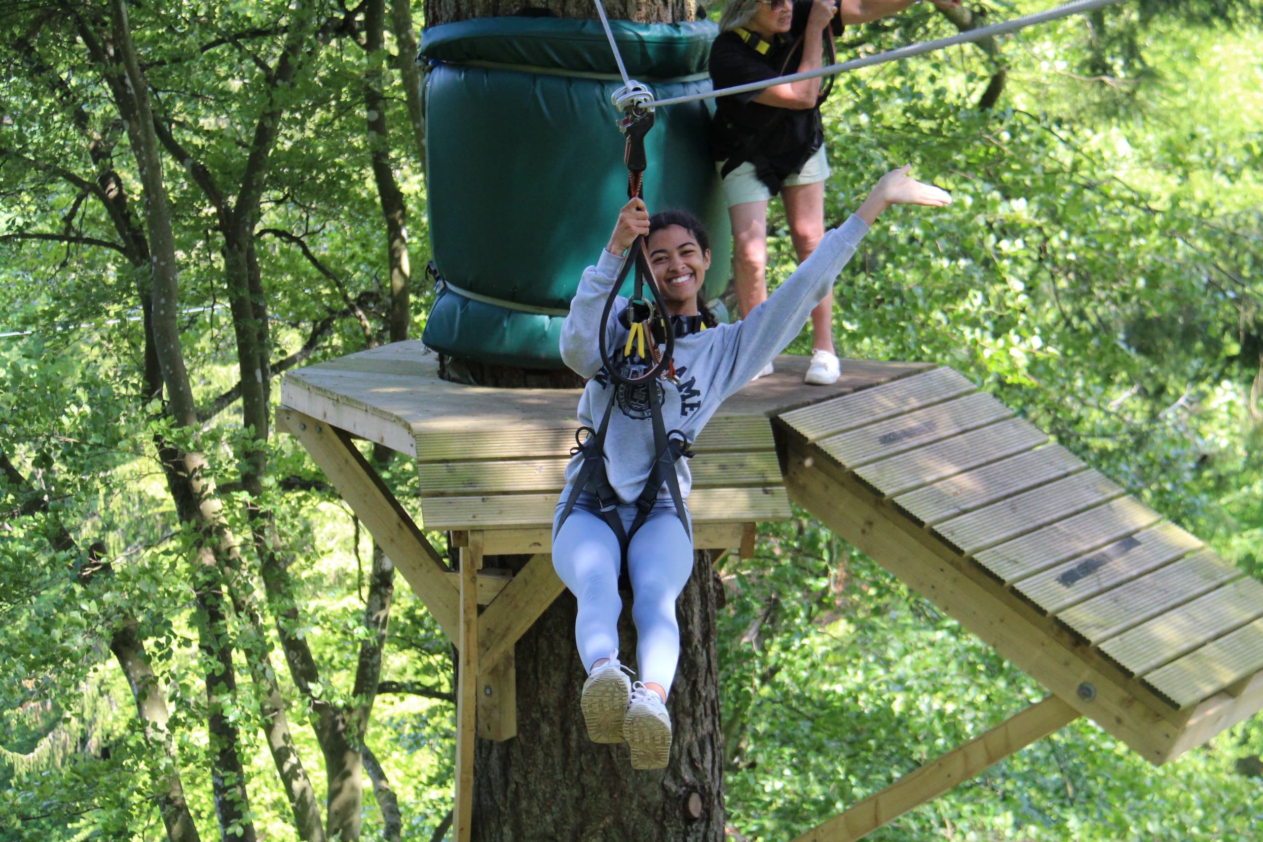 Participant ziplining from wooden platform through forest canopy