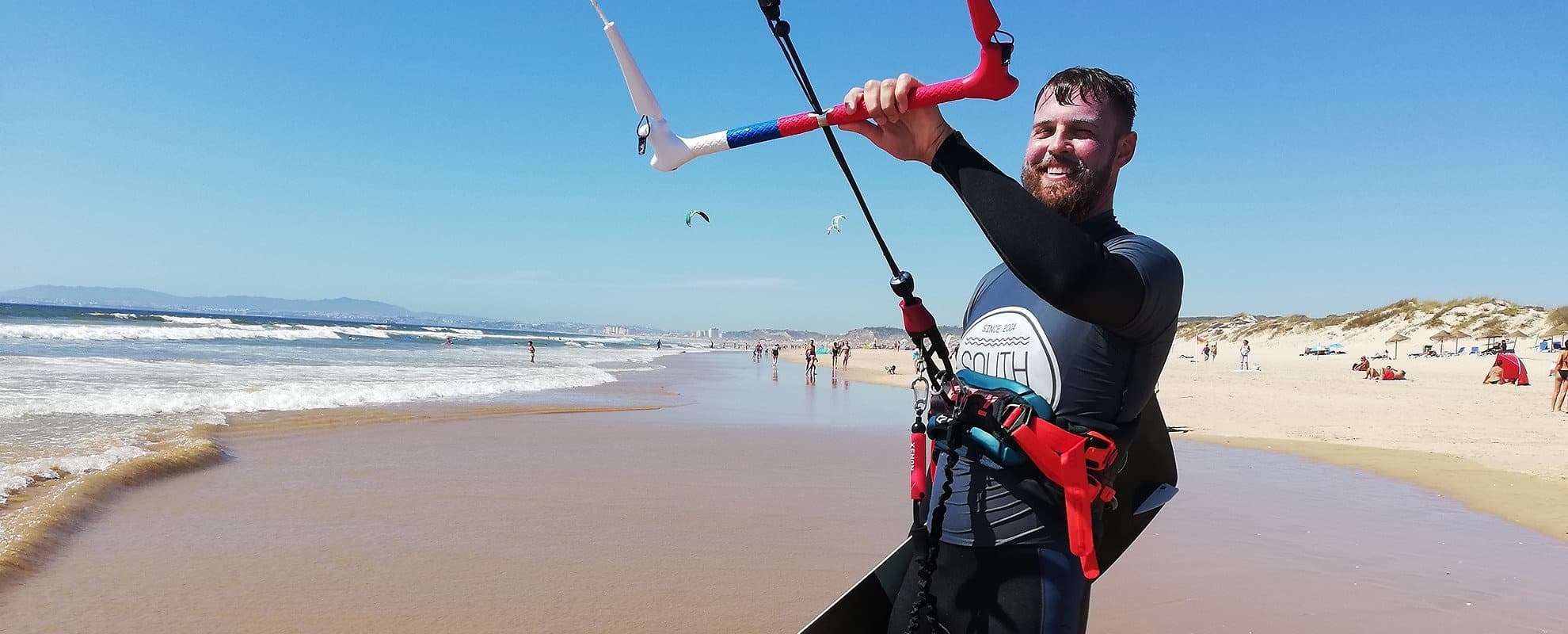 Kitesurfer launching kite on sunny sandy beach with waves