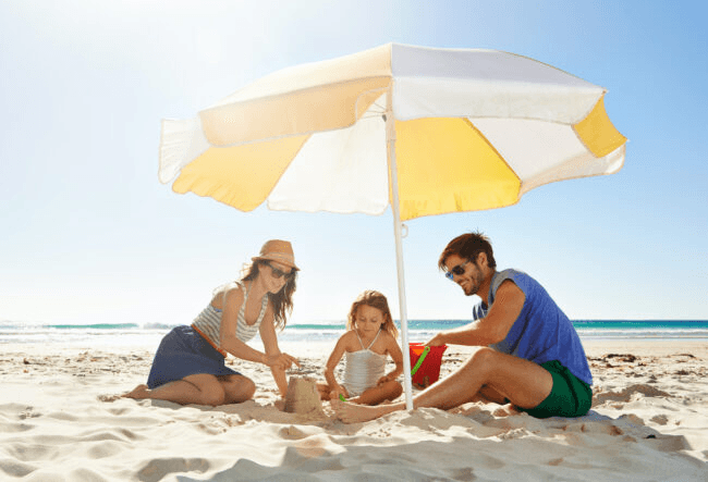 Family relaxing under umbrella on sunny tropical beach shoreline