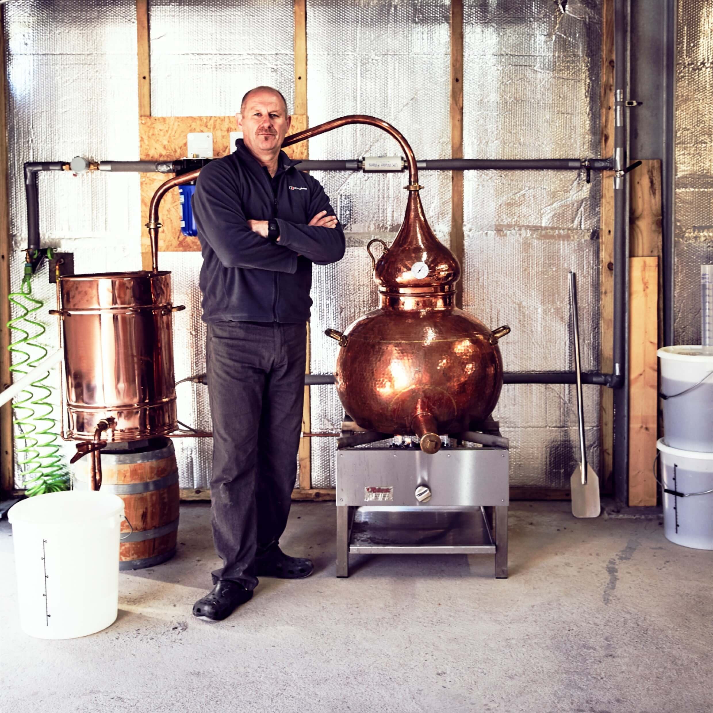 Distiller standing by copper still in indoor craft distillery tour