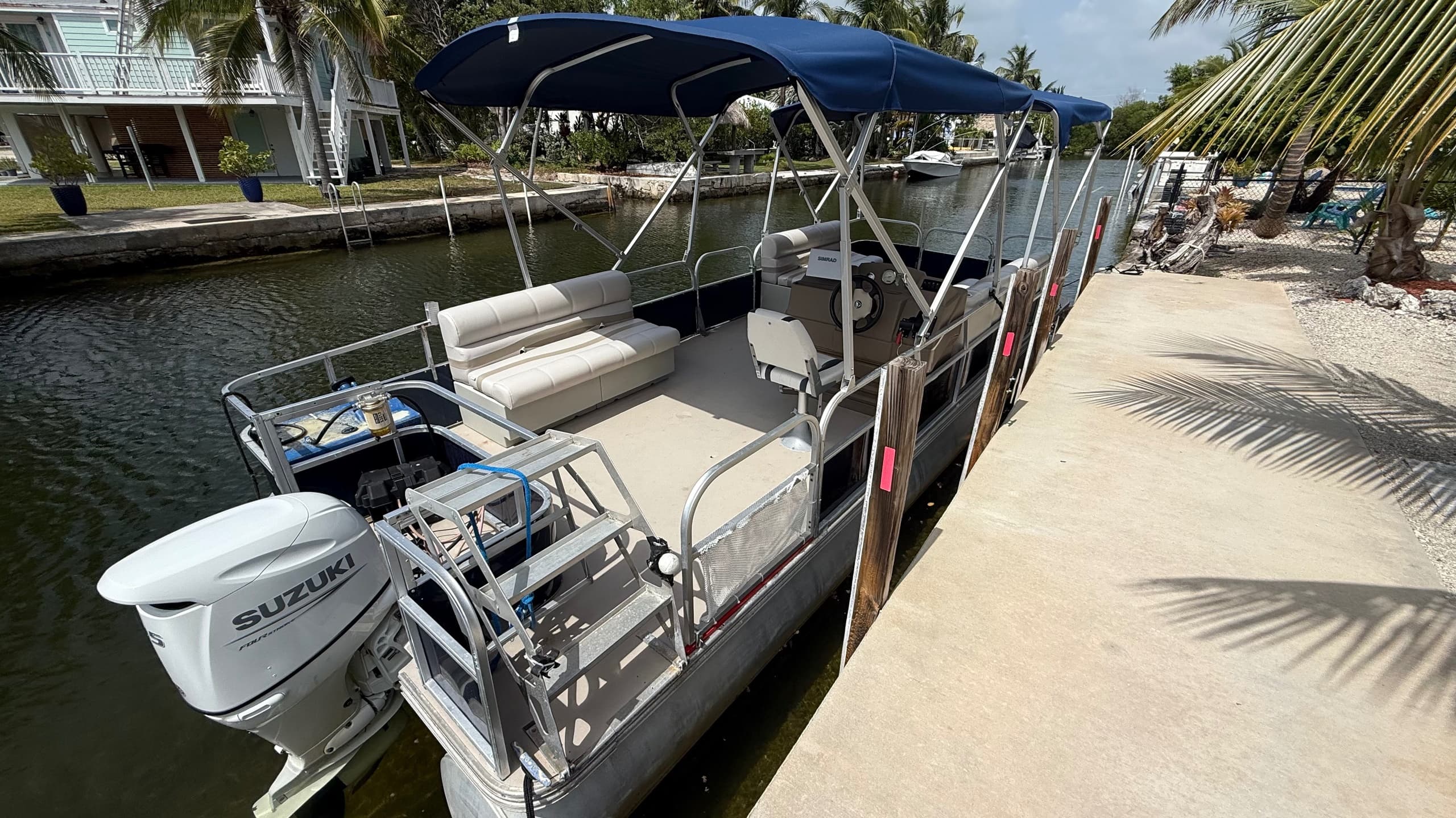 Pontoon boat docked along palm-lined canal, calm waterfront stay