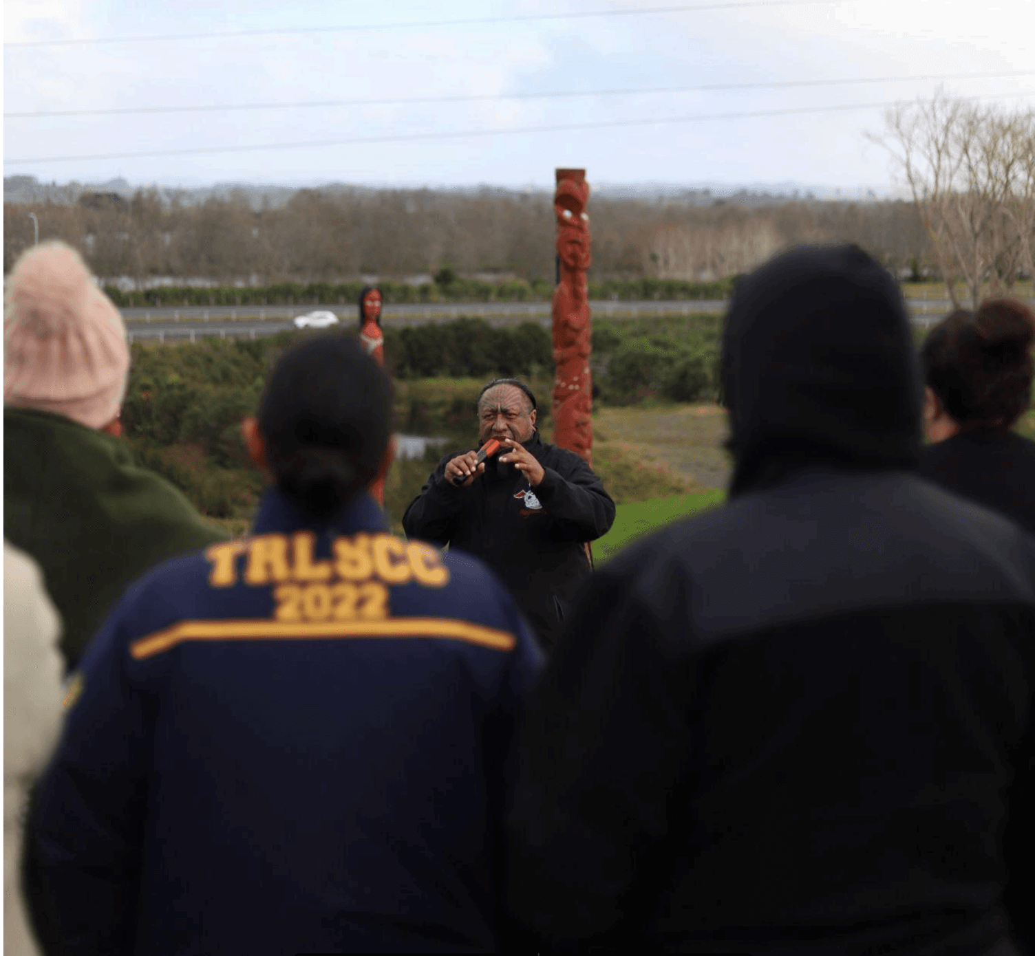 Outdoor cultural ceremony with speaker by carved totem