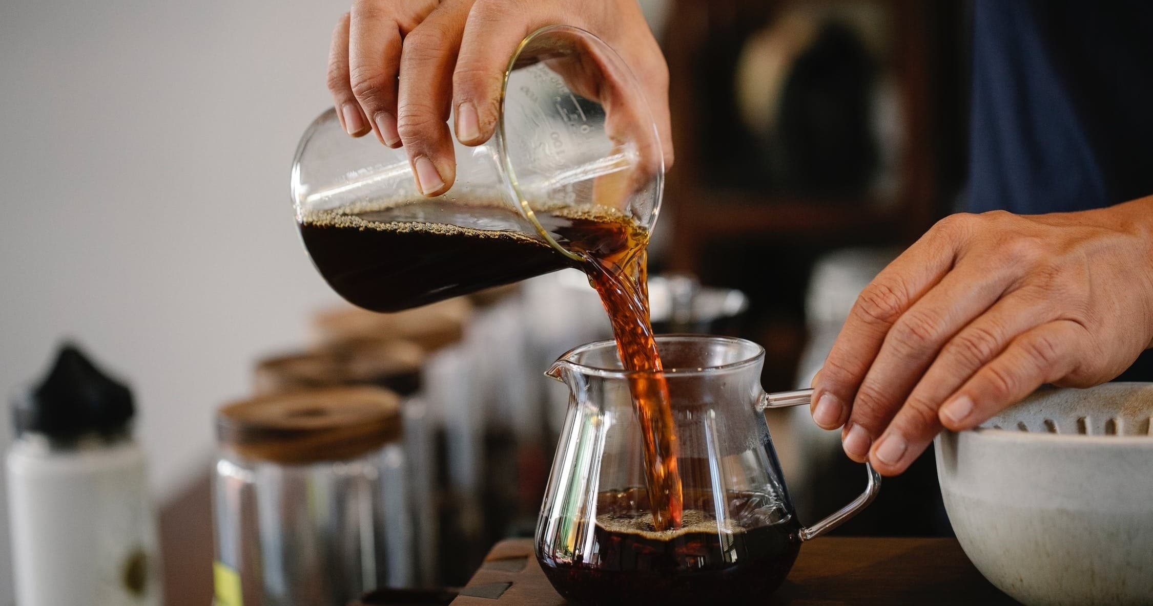 Barista pouring brewed coffee into glass carafe in café