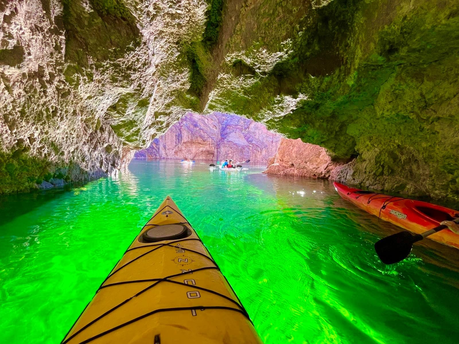 Kayaker paddling through glowing green sea cave, canyon inlet