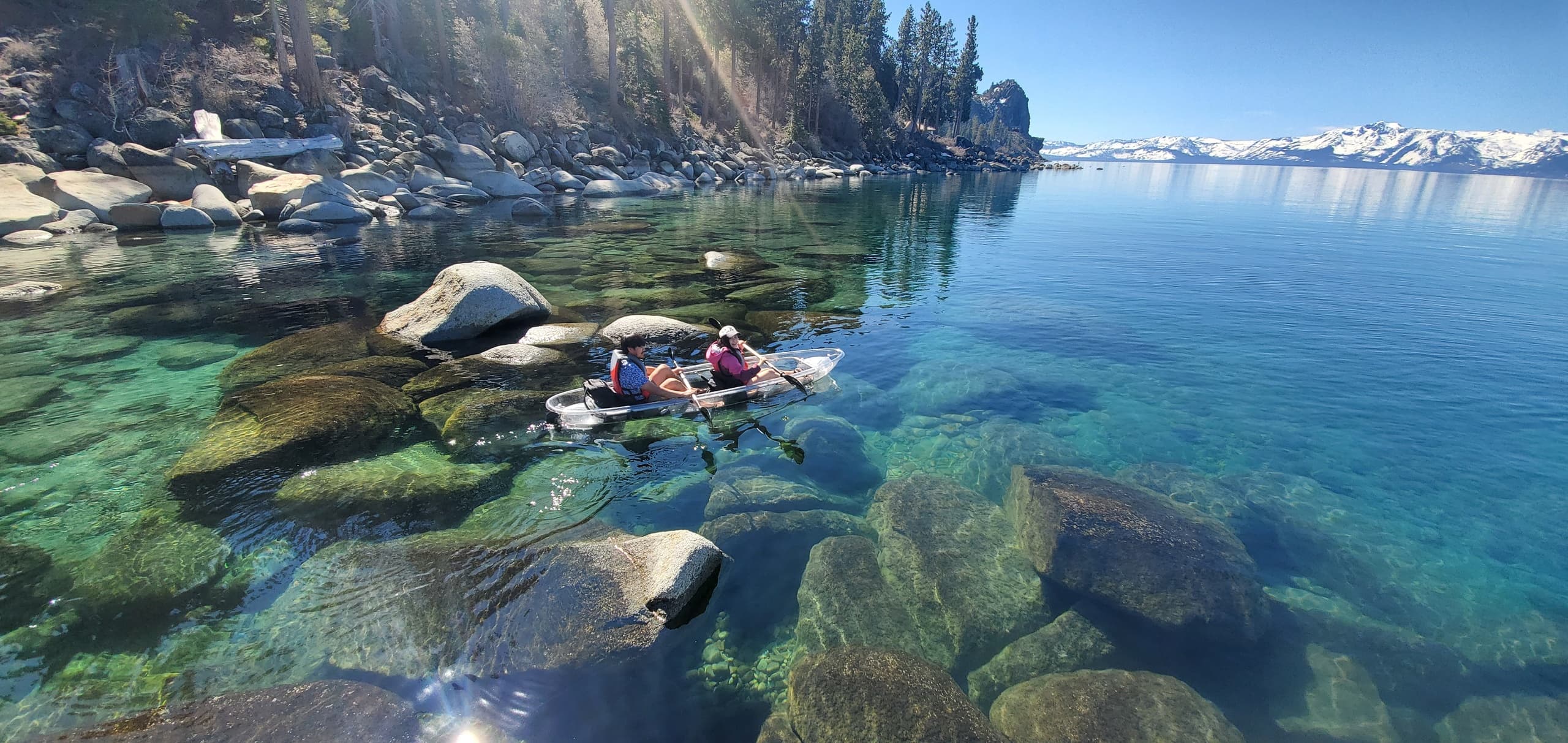 Kayakers paddling clear waters along Lake Tahoe rocky shoreline