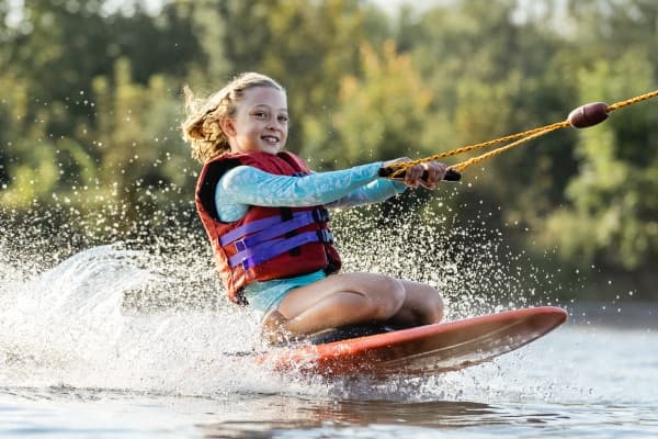 Young girl wakeboarding with towline on scenic lake in Zossen
