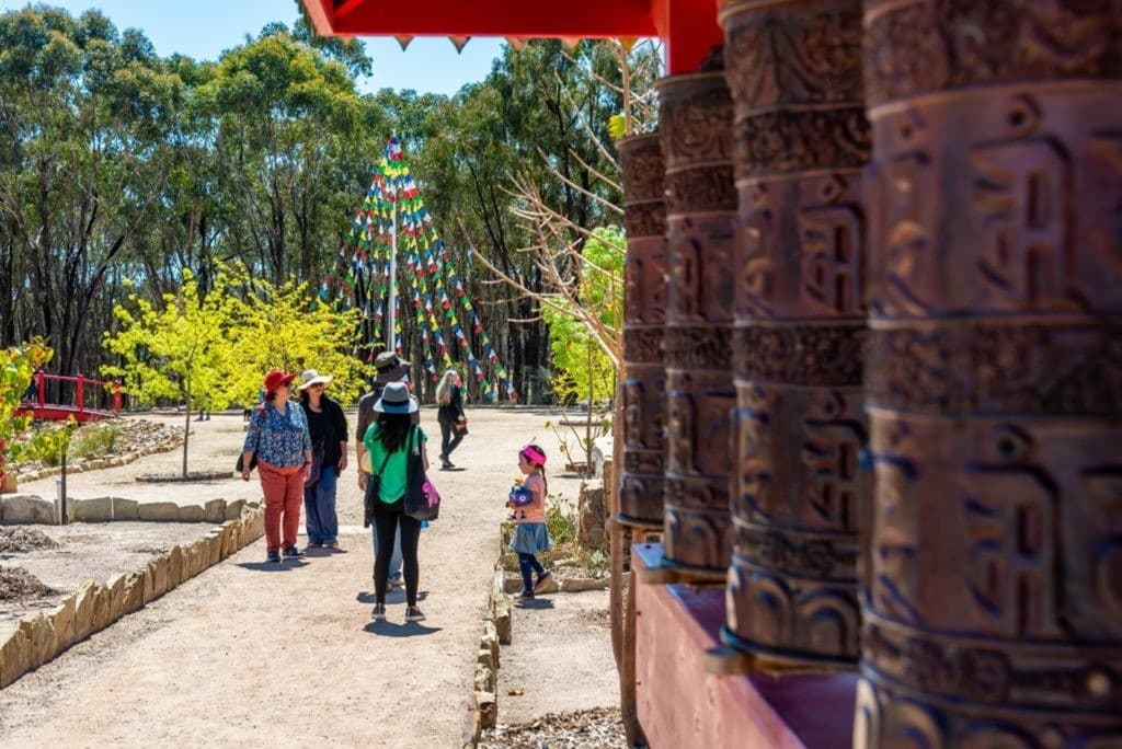 Prayer wheels lined along pathway with visitors in stupa gardens