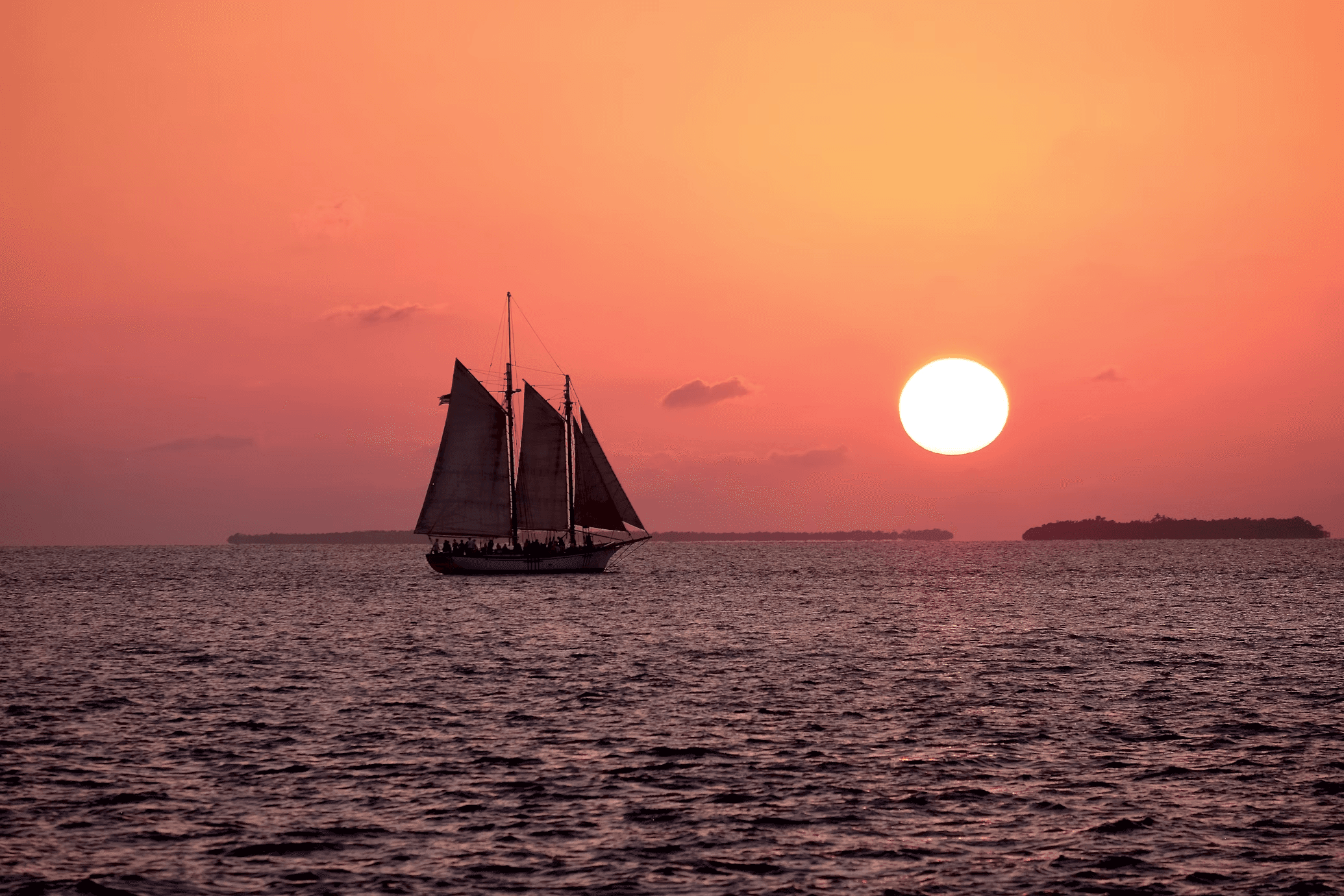 Sailing schooner silhouetted at sunset over open ocean cruise