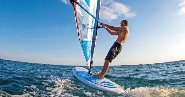 Windsurfer carving waves on open ocean with blue sky backdrop