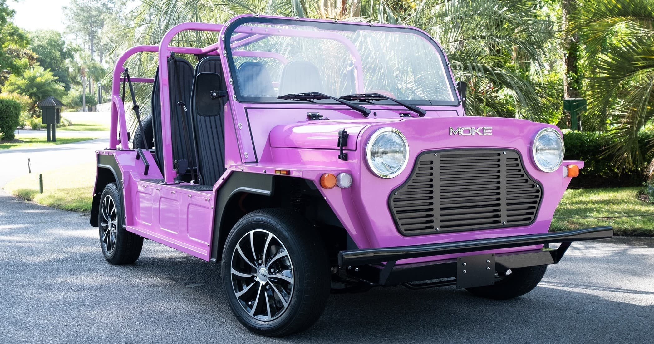 Open-top pink Moke parked on tree-lined road for scenic drives