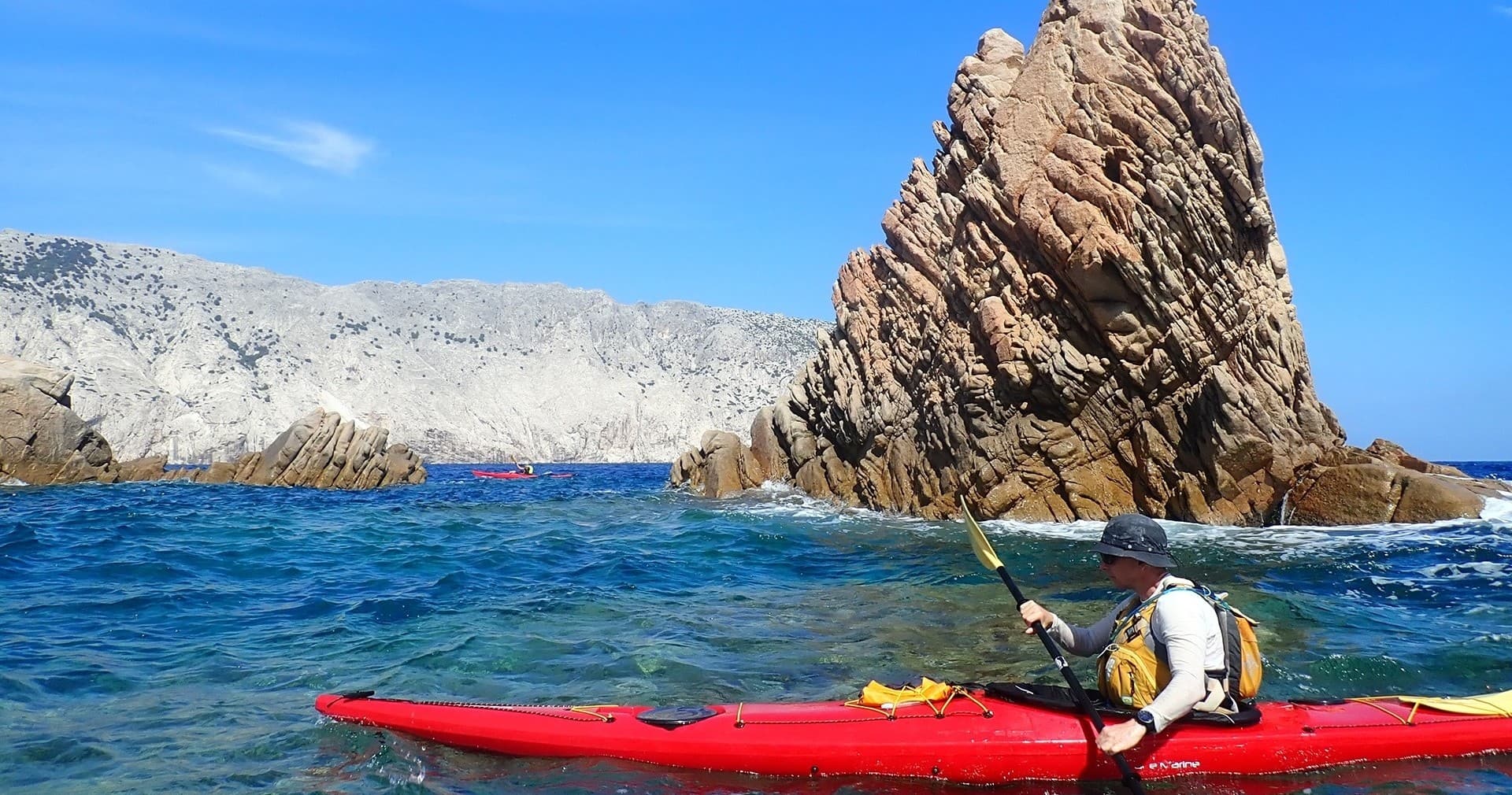 Solo kayaker paddling beside towering coastal rock formation