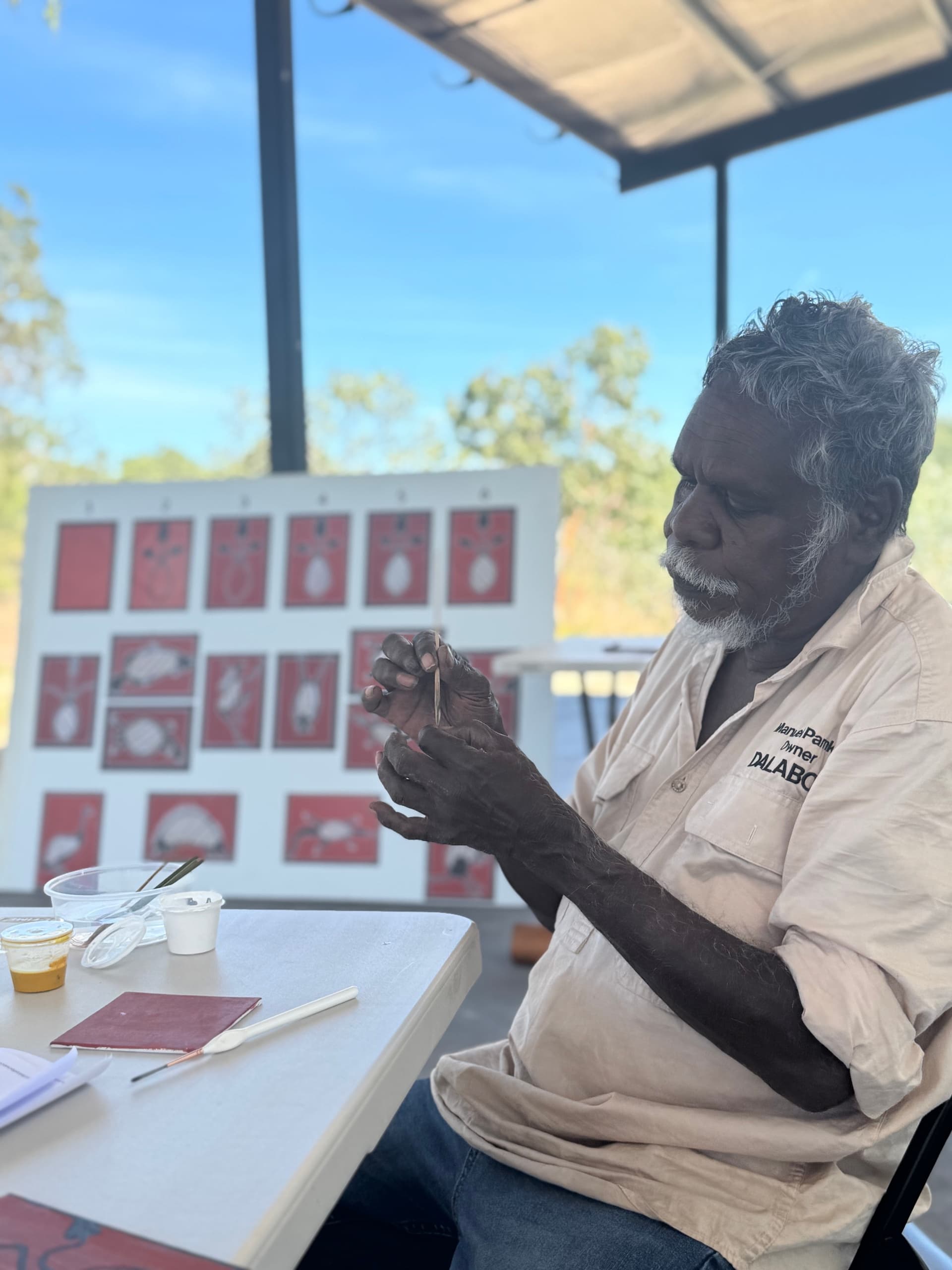 Aboriginal artist demonstrating dot painting outdoors at workshop