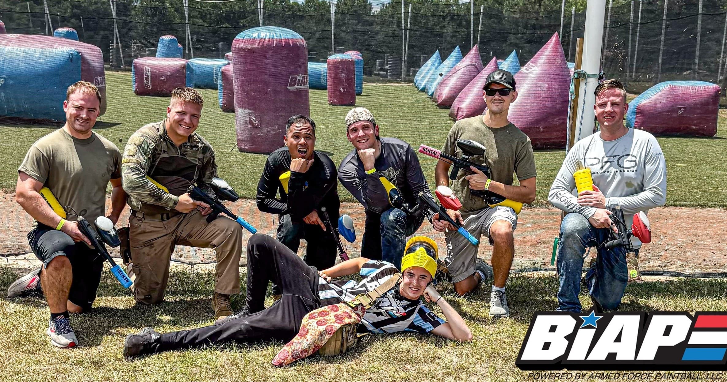 Mixed team posing on paintball field with inflatable bunkers