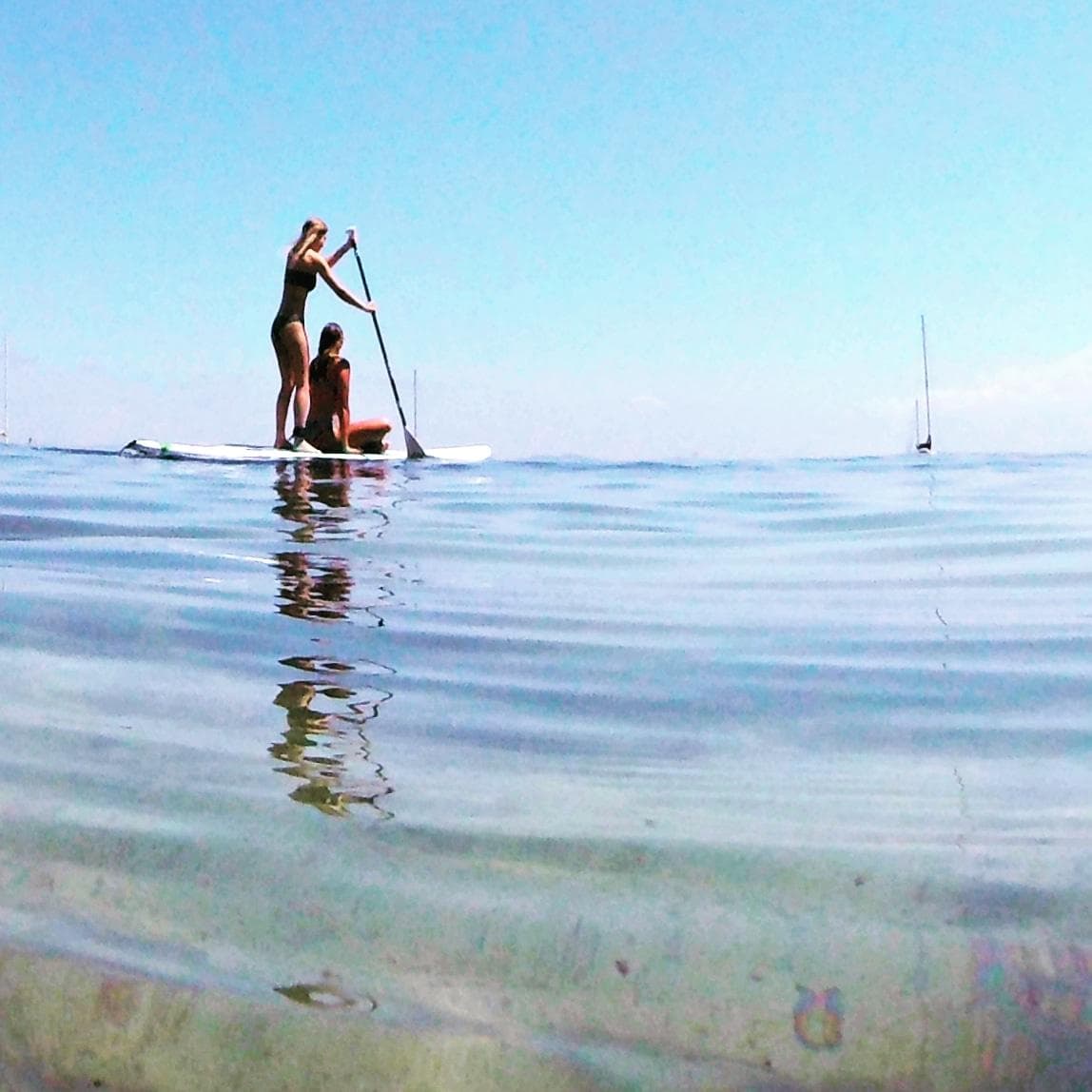 Couple stand-up paddleboarding on calm clear sea with reflections