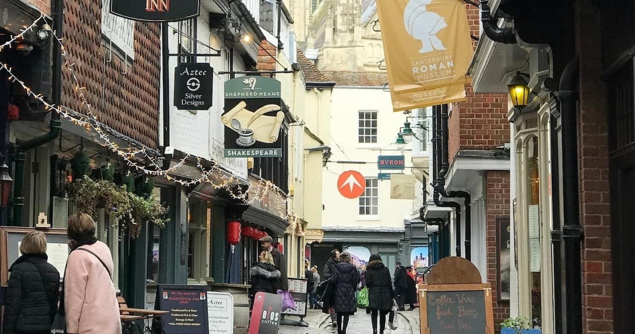 Cobblestone Canterbury lane with shops and running tour groups