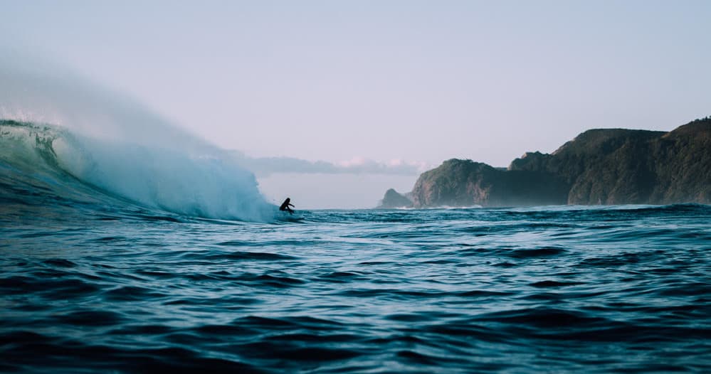 Surfer riding large ocean wave with coastal cliffs in Maui