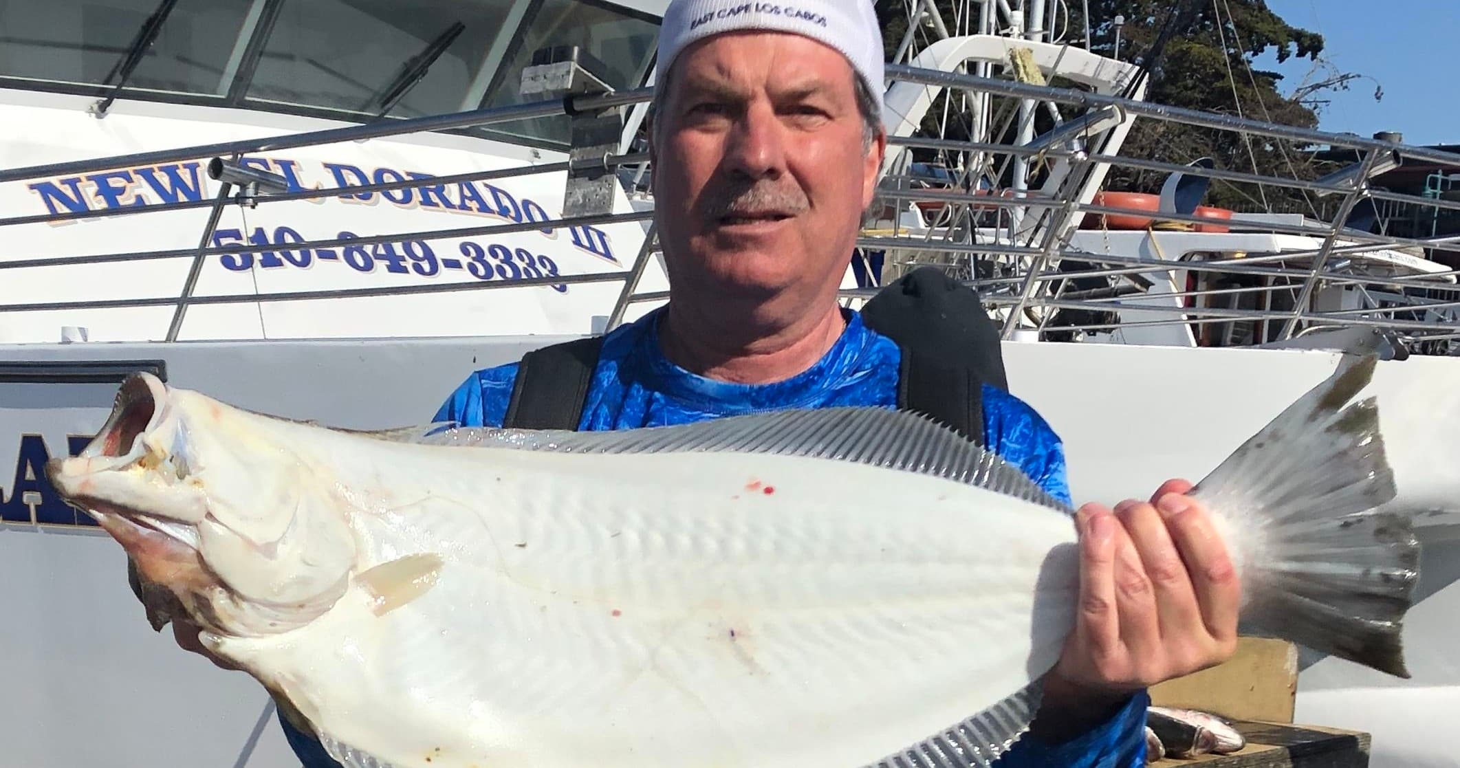 Angler holding large halibut on dock in marina, fishing charter catch