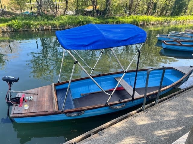 Small blue canopy boat moored at riverside dock with trees