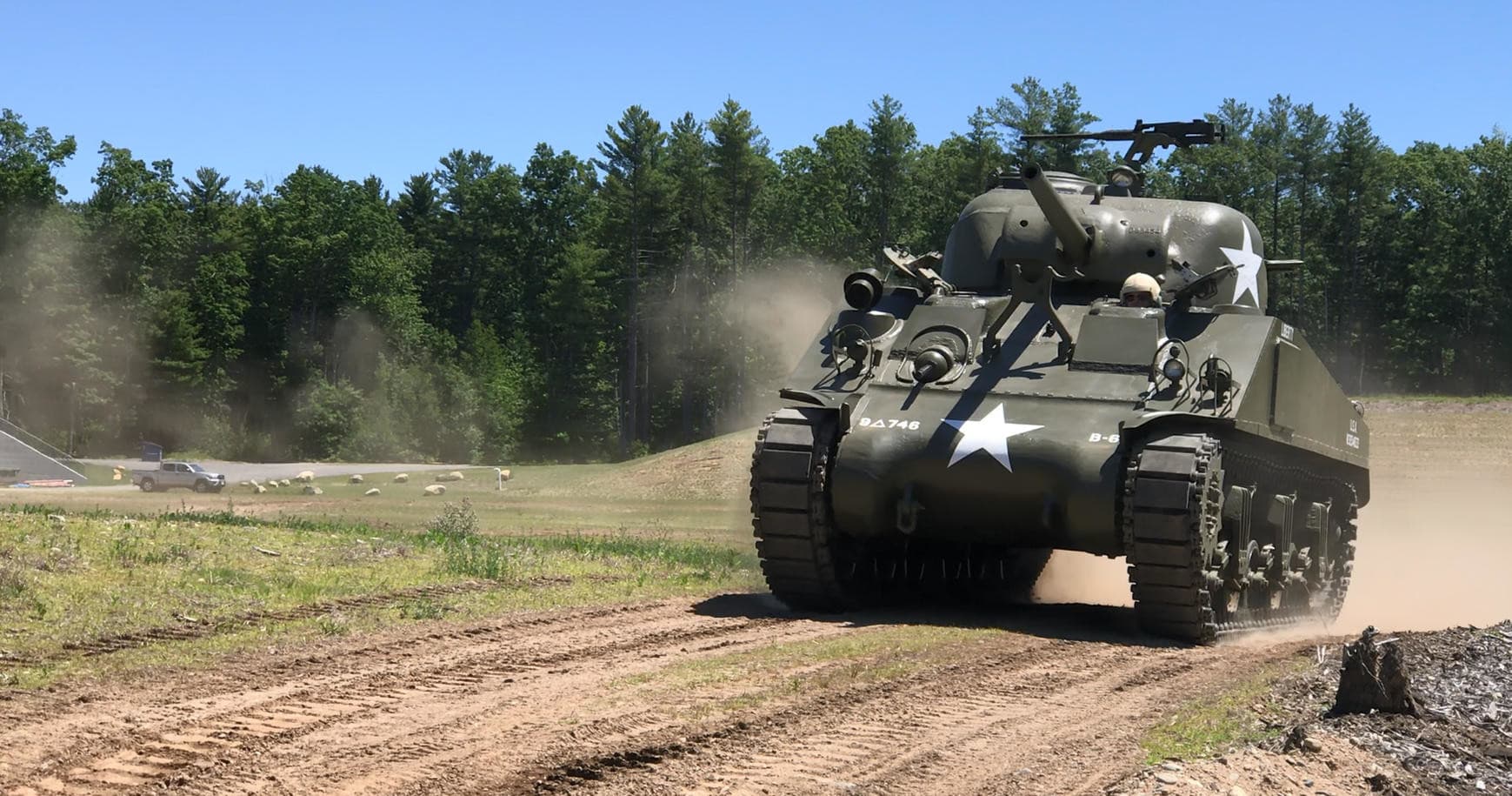 WWII M4 Sherman tank driving on dusty trail through woods