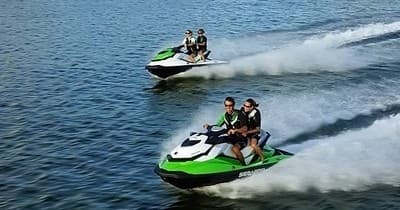 Two riders jet skiing across open ocean waters at high speed