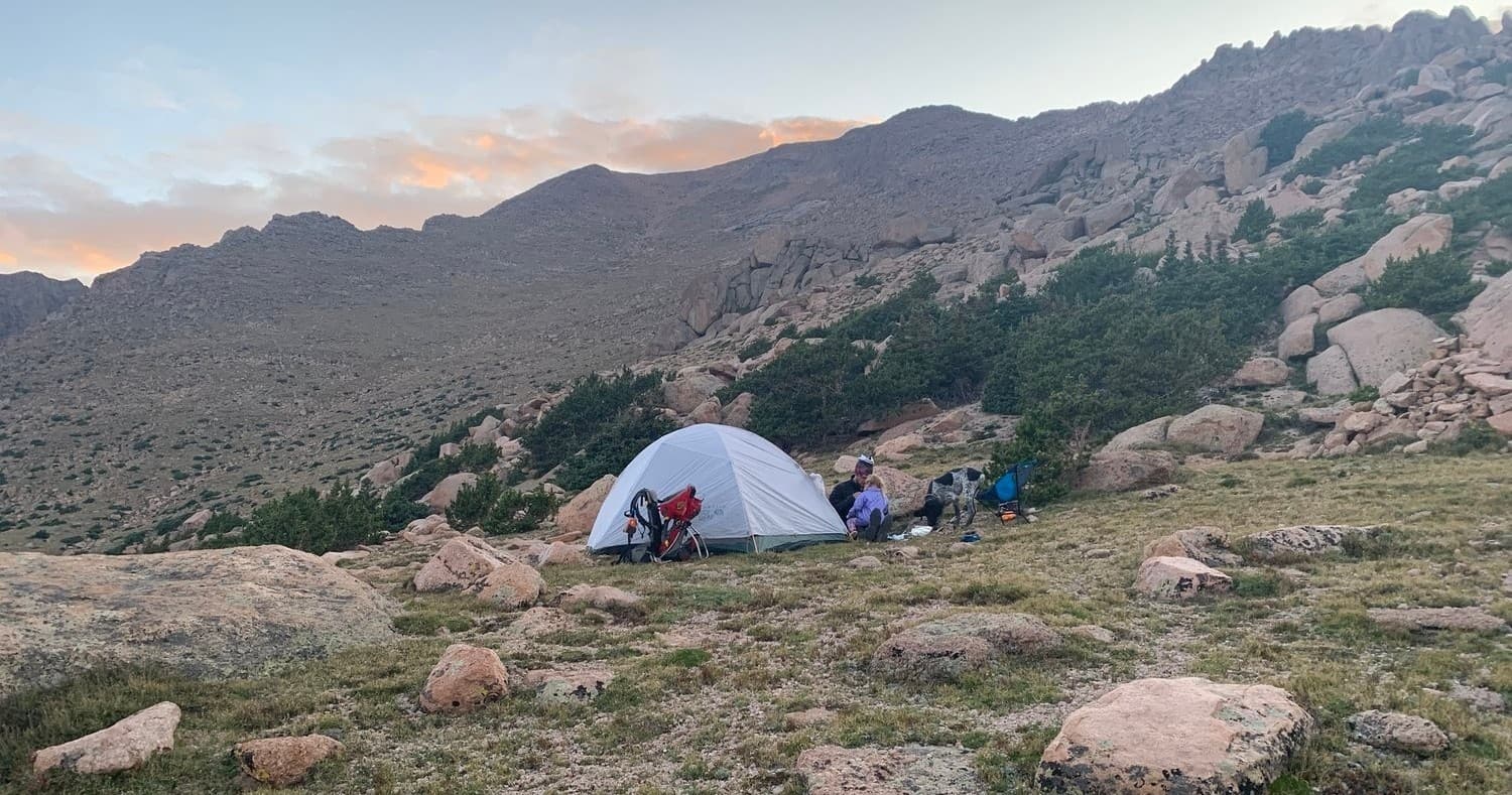 Backcountry campsite with tent amid alpine tundra at sunset
