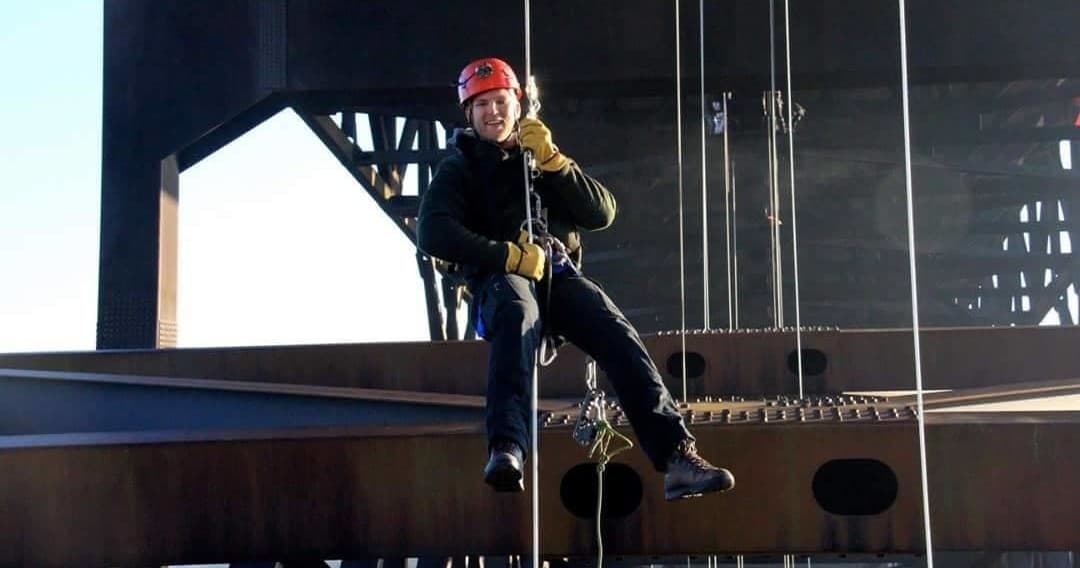 Climber rappelling off urban steel bridge, safety gear visible