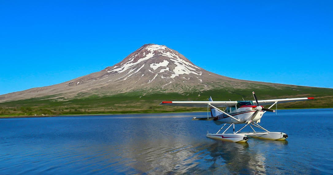 Seaplane landing on alpine lake with volcanic peak backdrop
