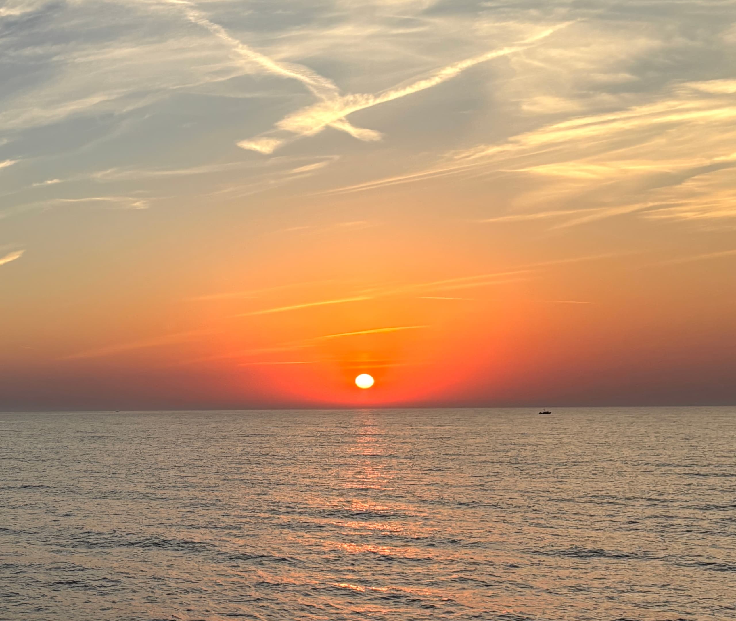 Sunset over open sea with vibrant orange sky and calm water
