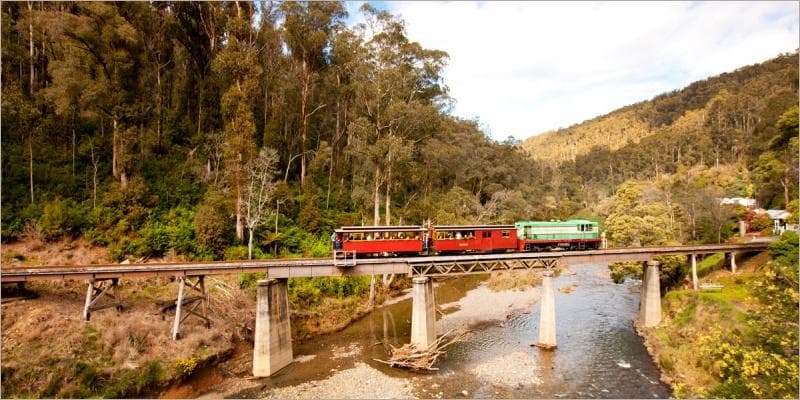 Scenic heritage train crossing river bridge in forest valley