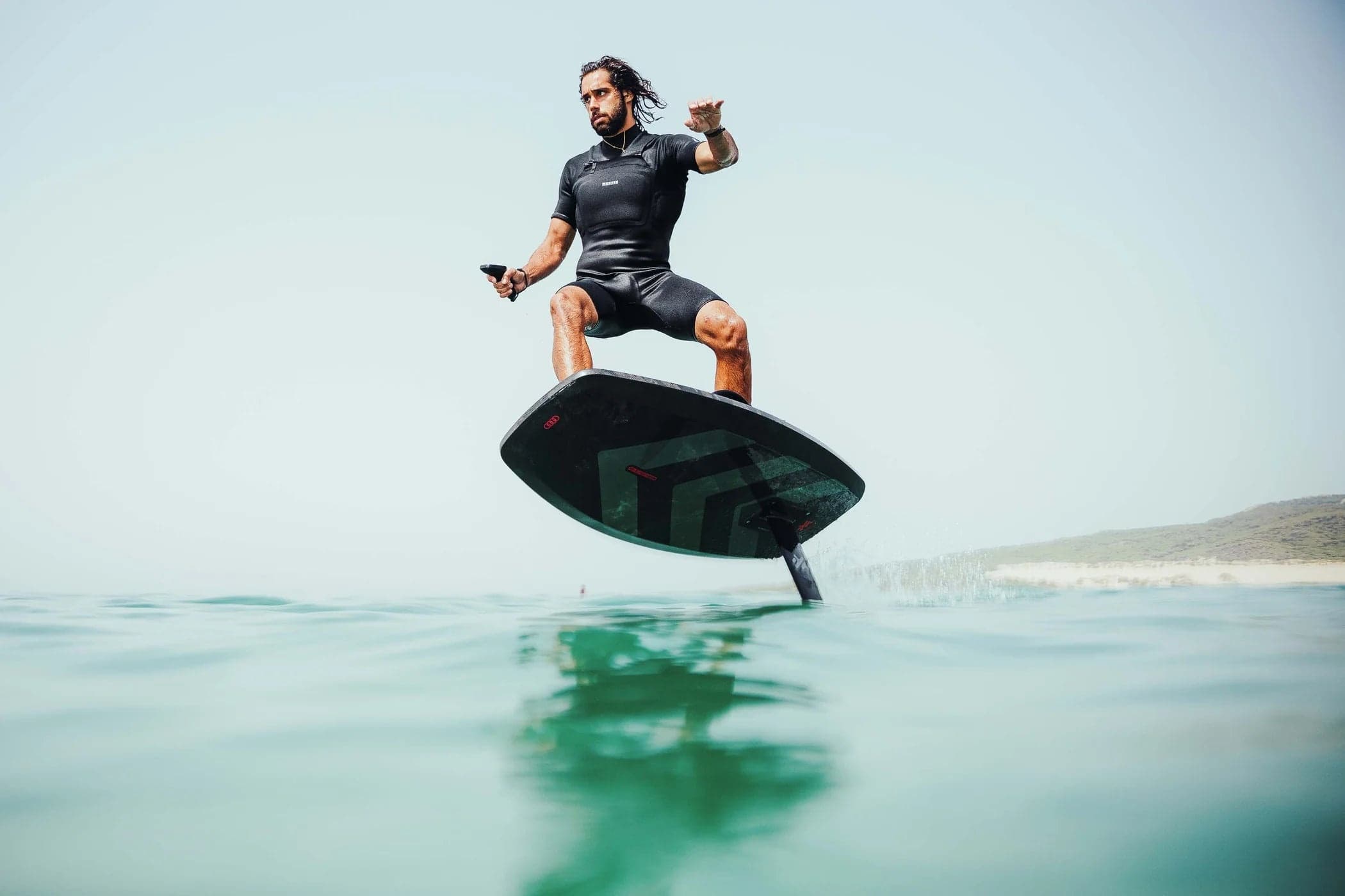 Male e-foil rider jumping over ocean swell near shore