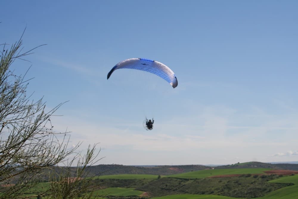 Solo paraglider soaring above green hills near Madrid, Spain