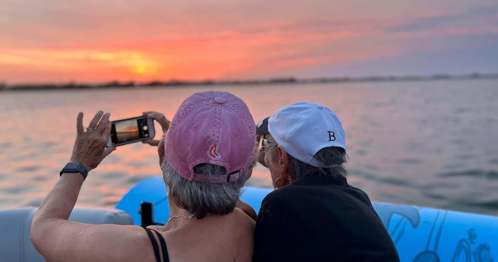Couple photographing sunset from inflatable boat on ocean