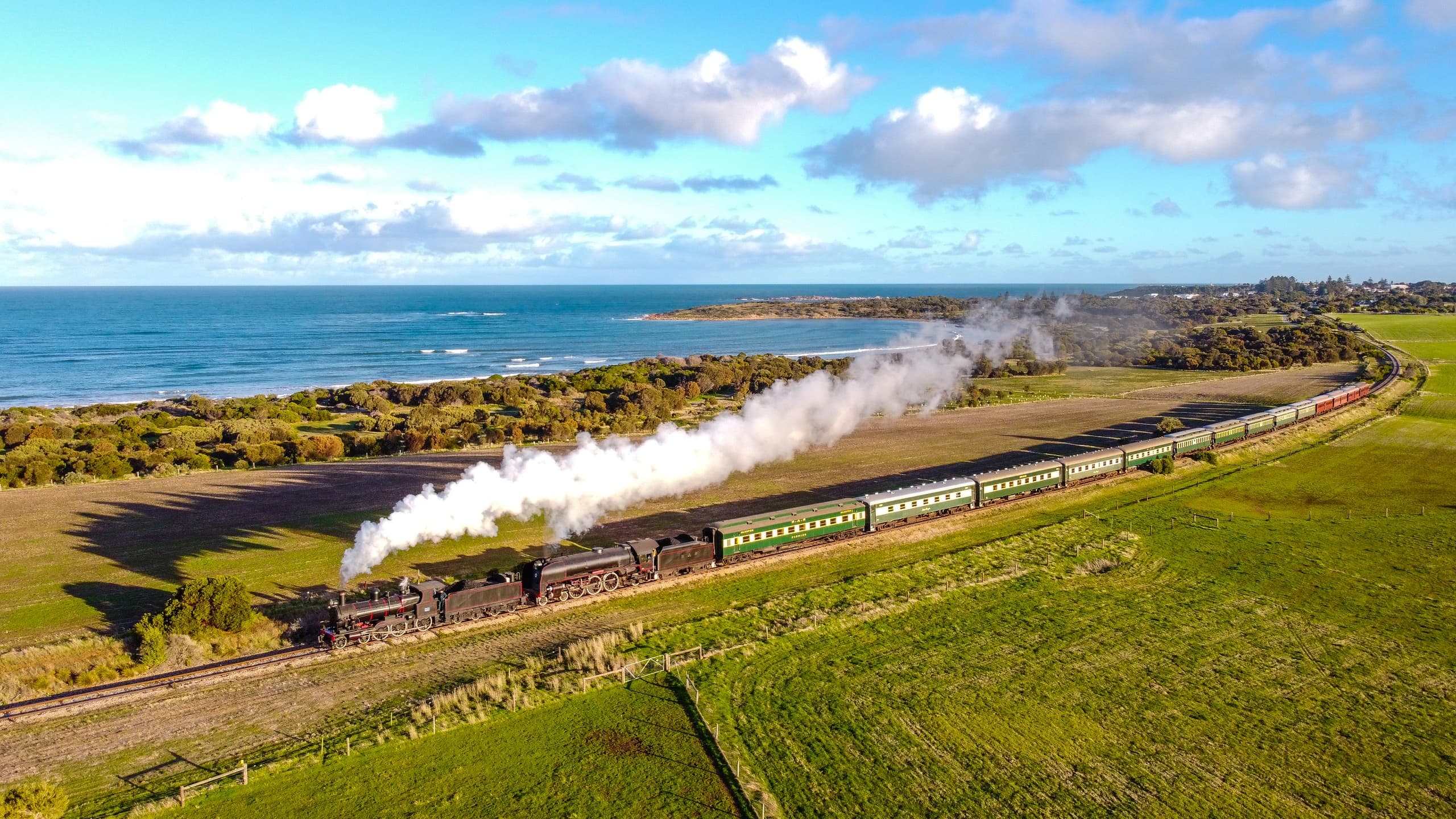 Steam train rounding coastal curve with billowing smoke, scenic