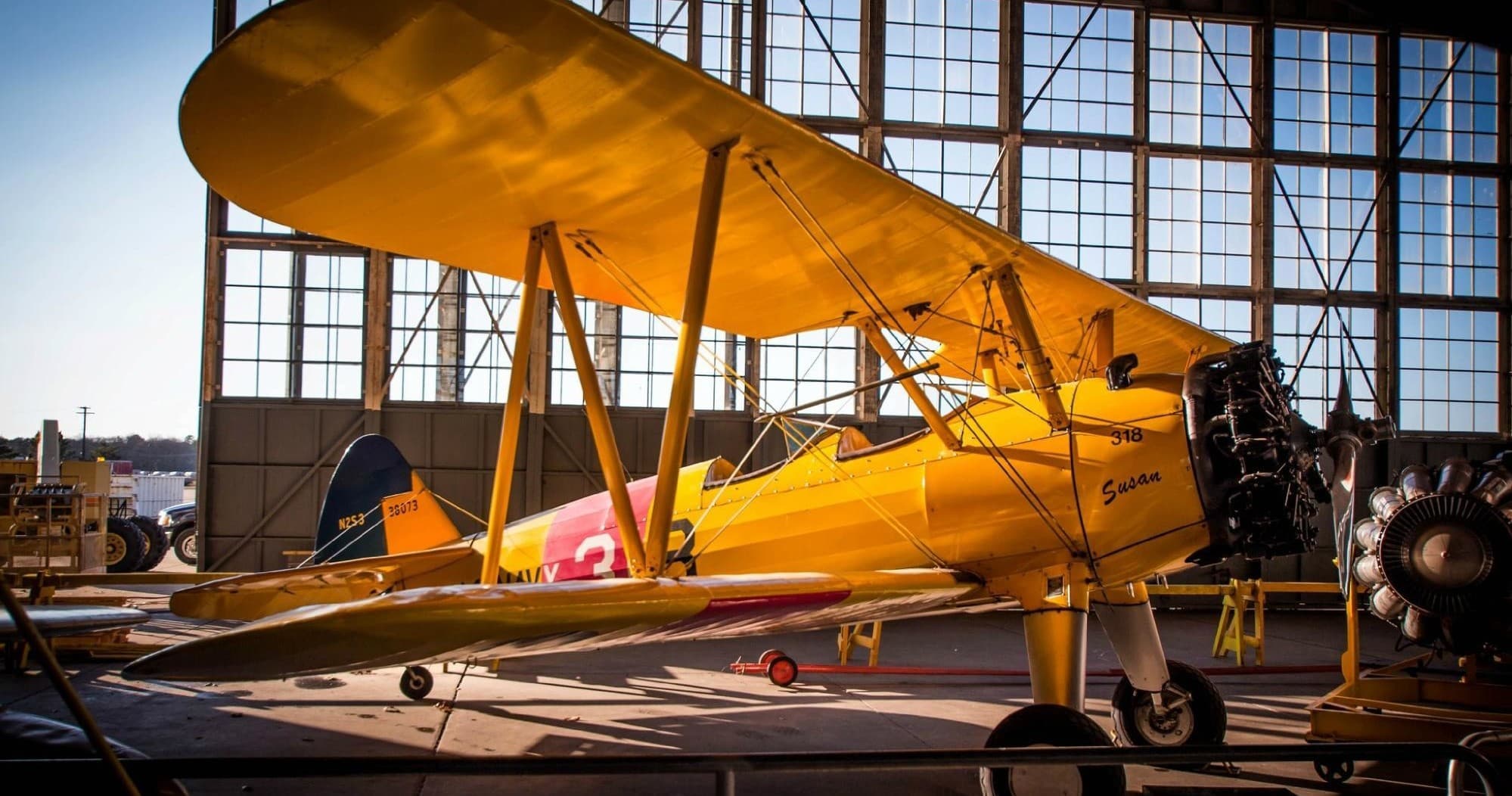 Yellow vintage biplane in hangar with sunlight, historic flight demo