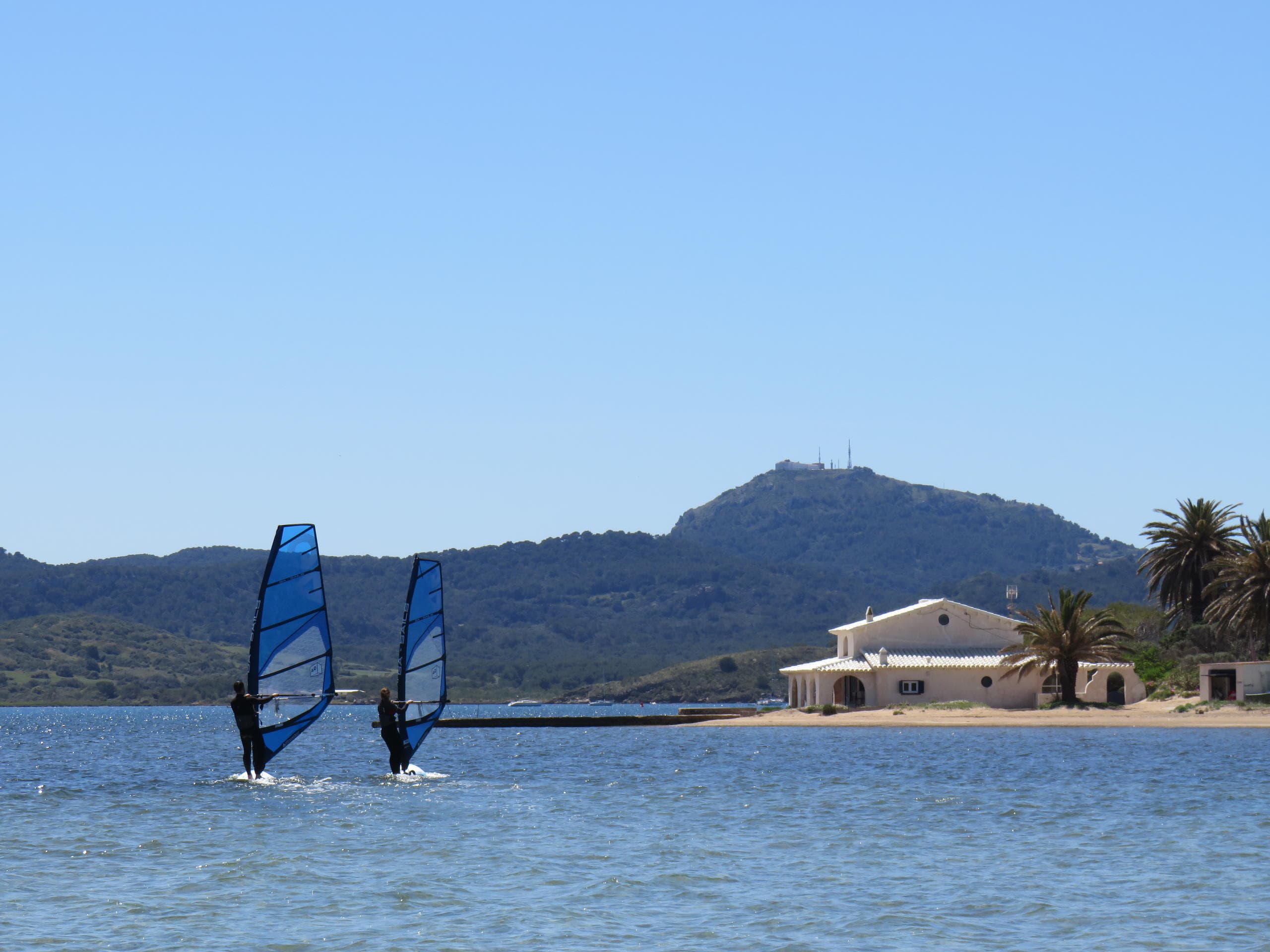Two windsurfers gliding in coastal bay with mountain backdrop